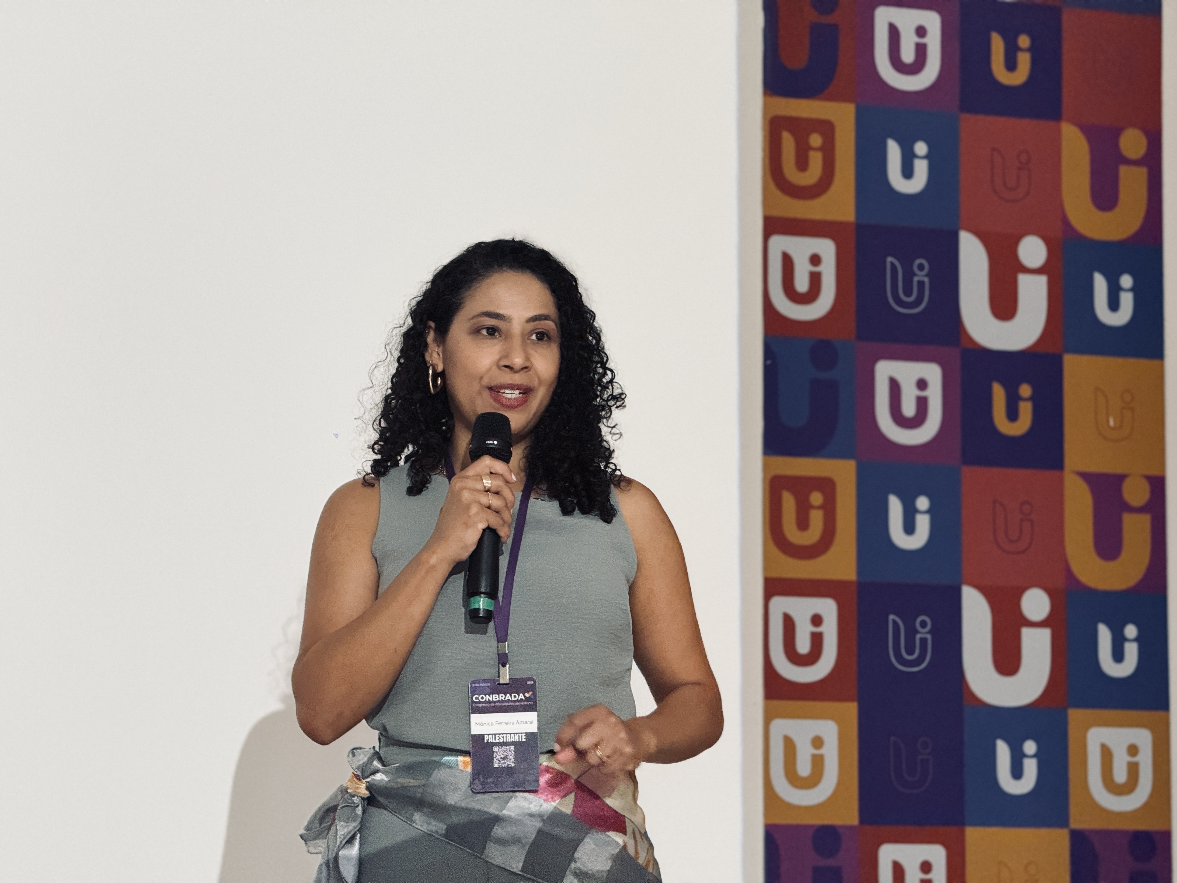 Mônica falando ao microfone em uma palestra