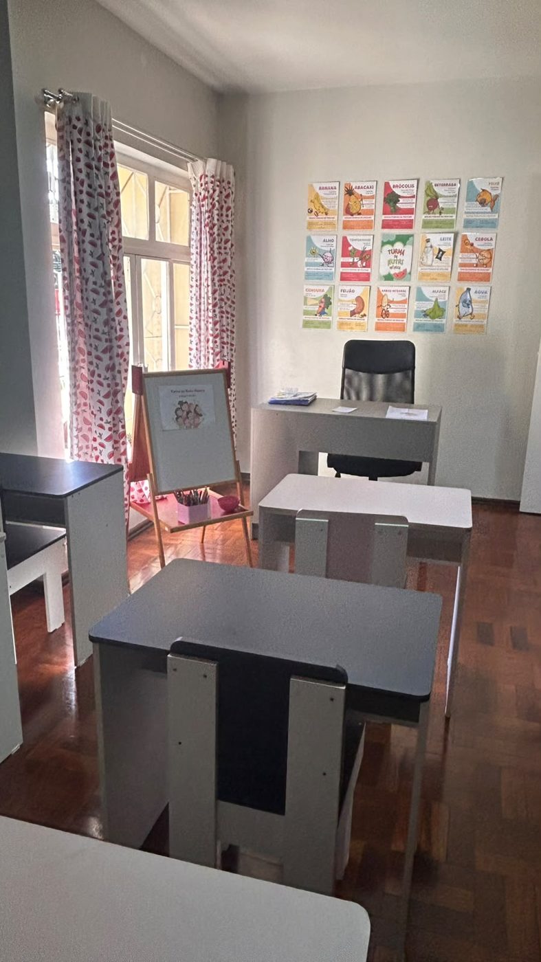 Sala da escolinha vista das mesinhas, com cartazes na parede