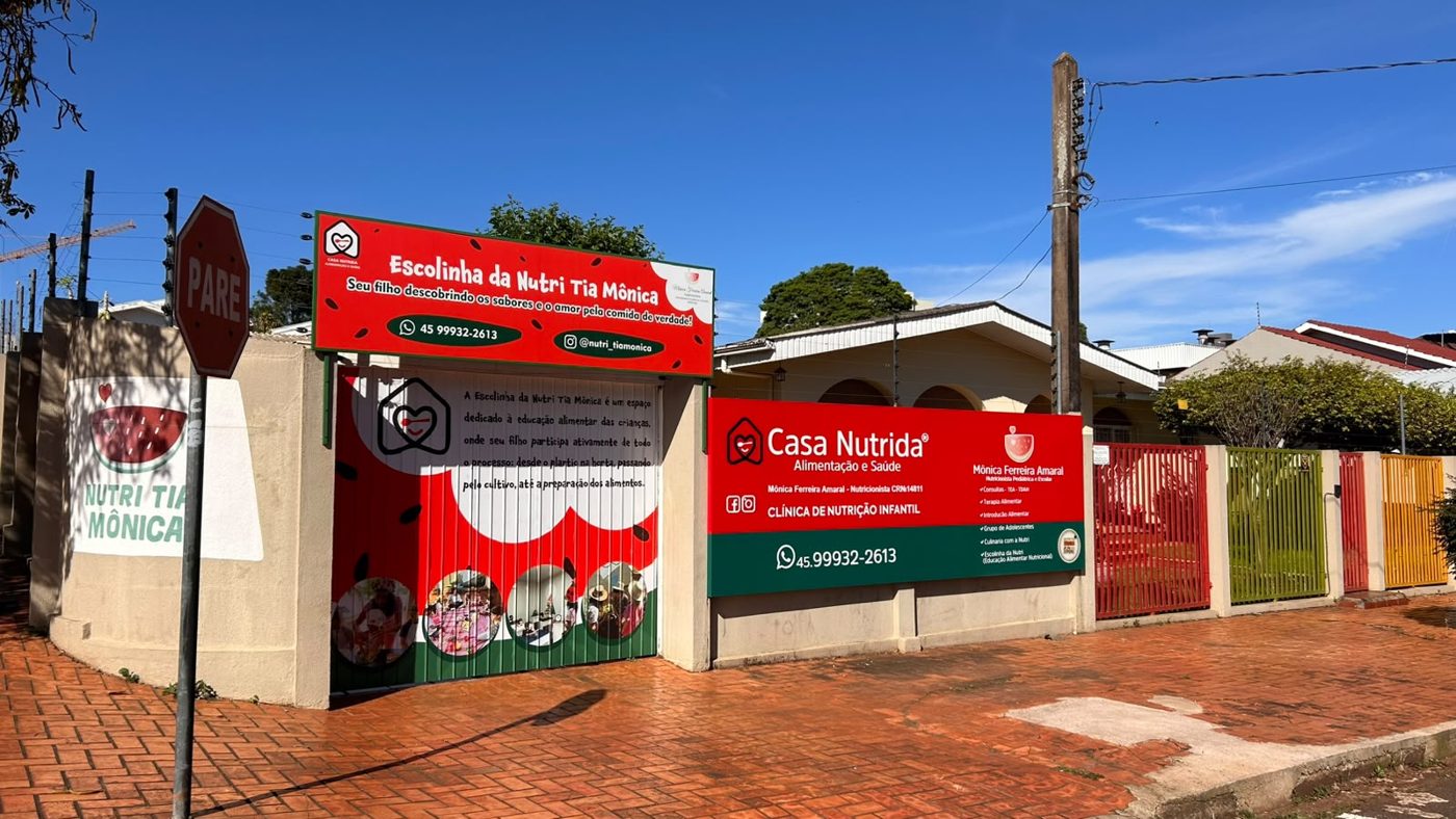 Fachada da Casa Nutrida com muro vermelho e placas da Escolinha da Nutri Tia Mônica