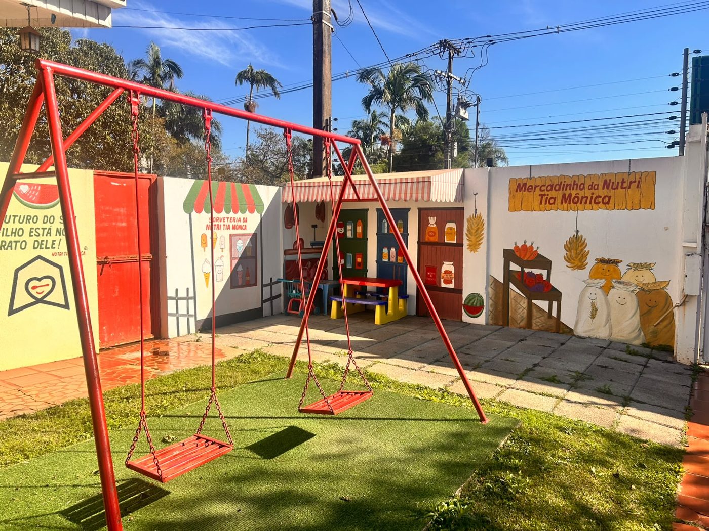 Parquinho com balanço vermelho, grama sintética e muro pintado