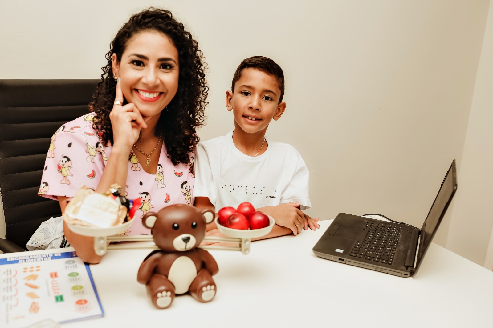 Mônica em atendimento com um menino, com alimentos sobre a mesa